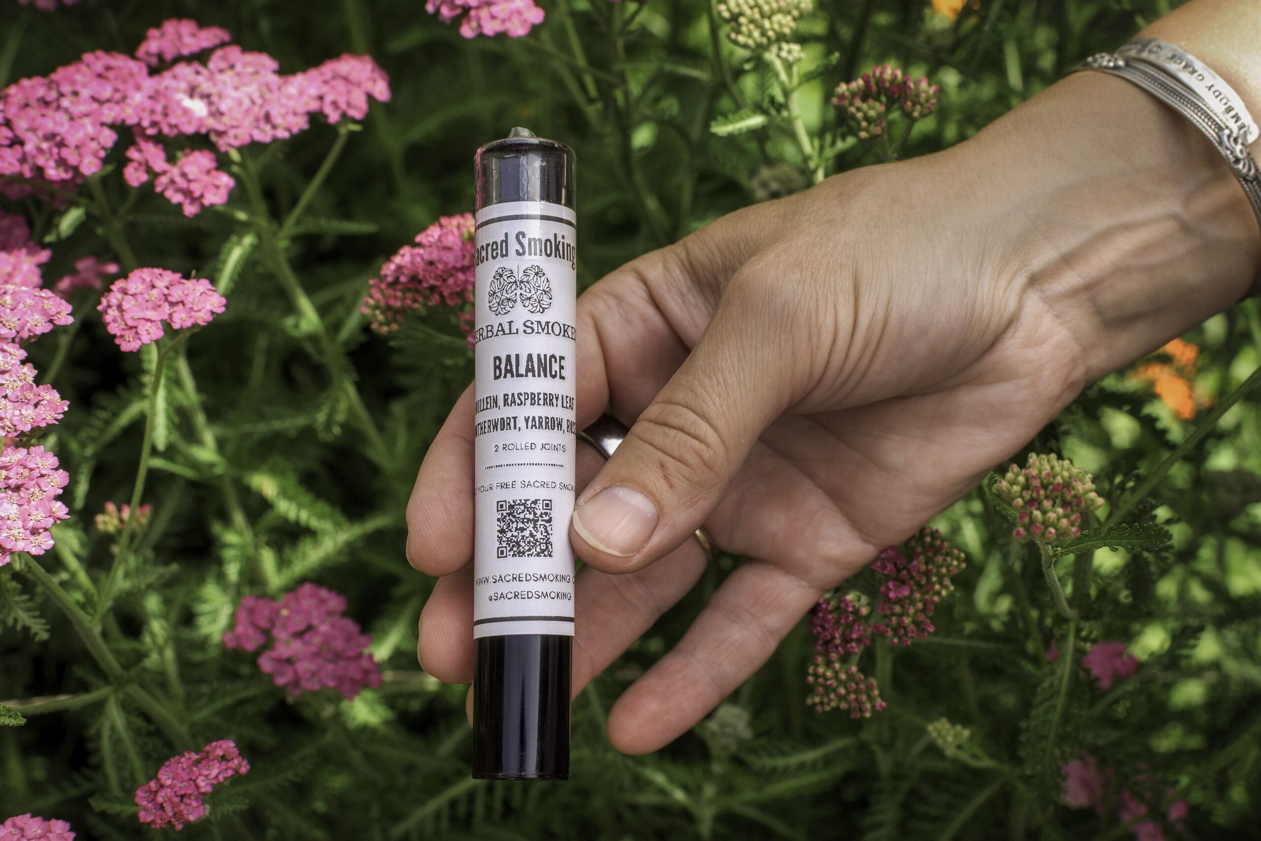 hand holding a tube of rolled joints in a bush of yarrow